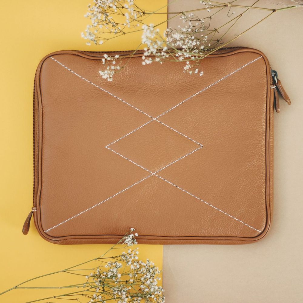 Top view of a stylish leather bag with stitching details on a pastel backdrop, decorated with white flowers